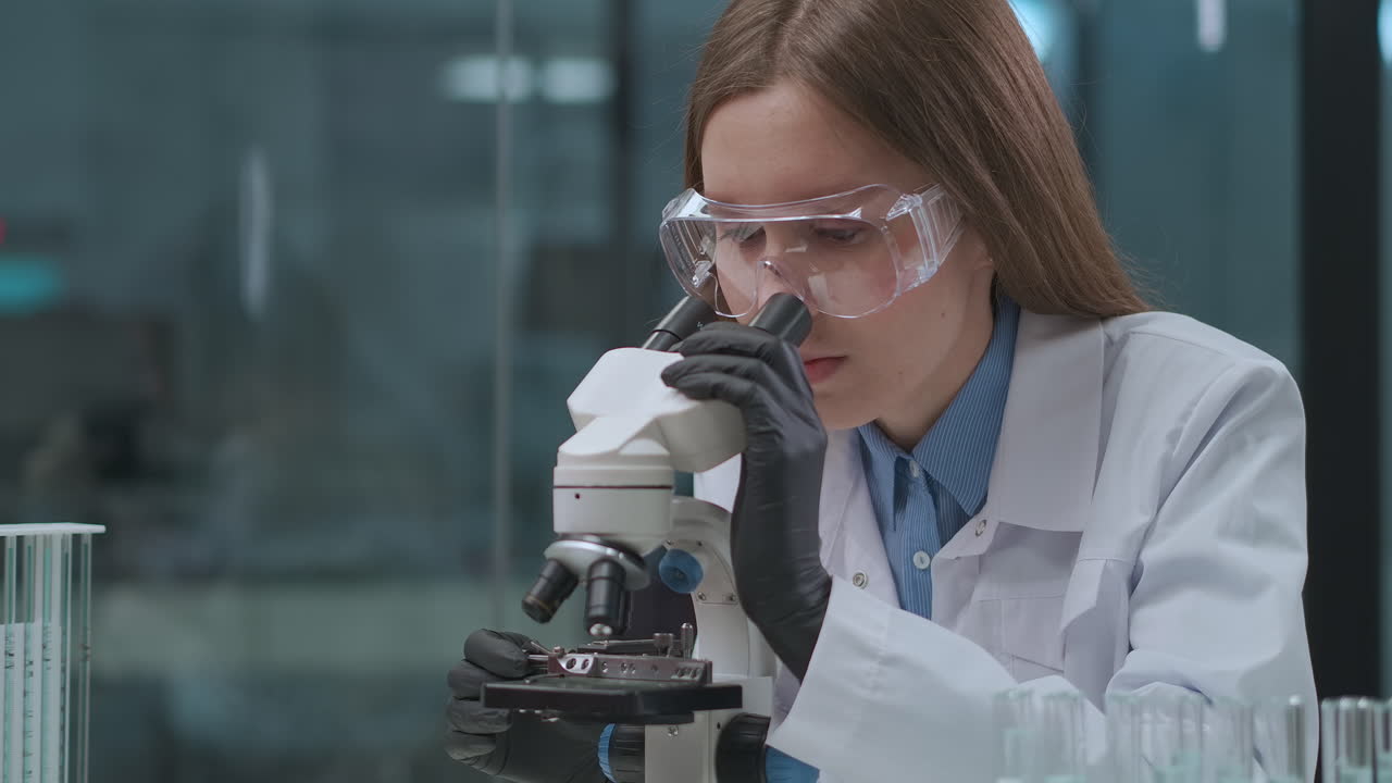 female virologist is exploring virus of covid-19 in medical laboratory viewing it in microscope research of coronavirus and looking for a curing
