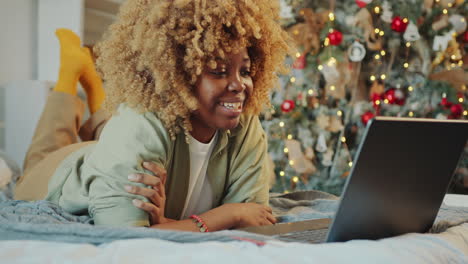 happy black woman video calling on laptop at home on christmas day