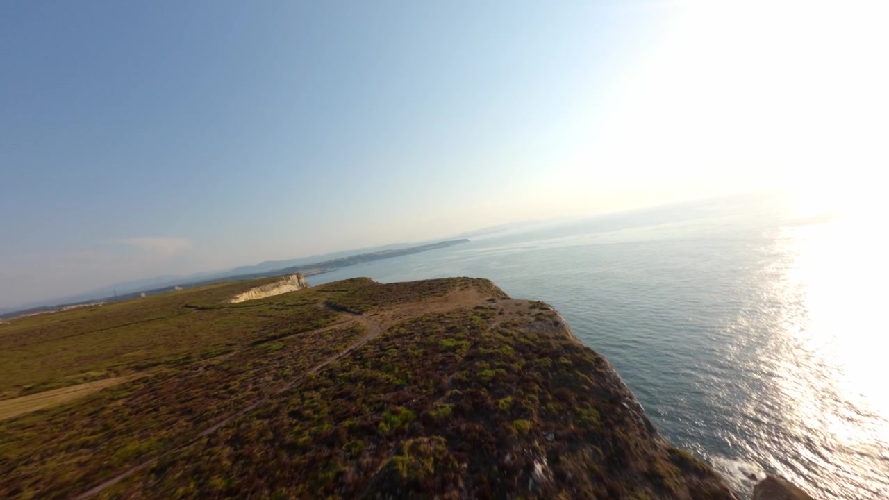 Ripresa aerea dinamica in stile FPV che scivola sulle aspre scogliere calcaree di Capo Peñas, nel punto più settentrionale della Spagna, con vista sul Mar Cantabrico durante l'ora d'oro.