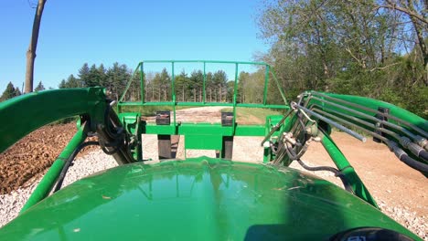 pov mientras opera un tractor verde con horquillas hidráulicas a lo largo