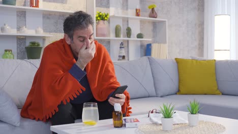 hombre maduro enfermo y perezoso usando su teléfono inteligente en casa, bebiendo bebidas saludables con vitaminas.