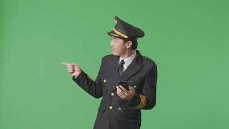 asian man pilot using smartphone and pointing to side while standing in the green screen background studio