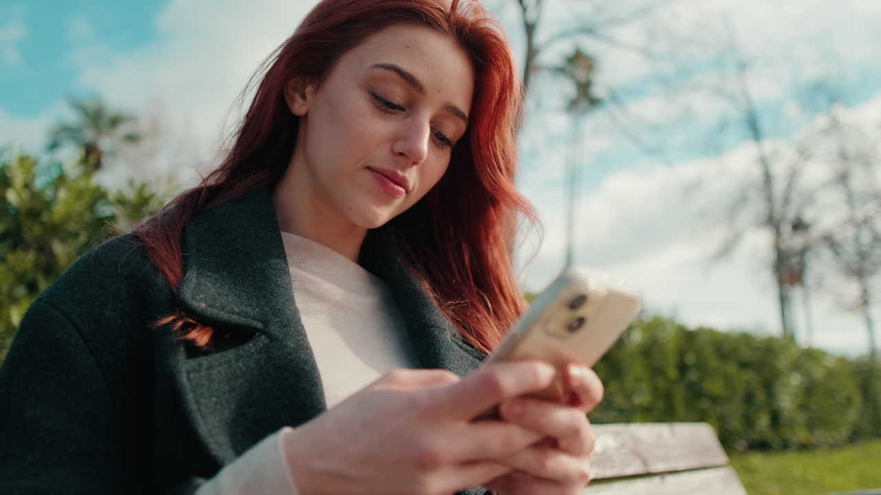 Giovane donna che sorride mentre usa lo smartphone al parco
