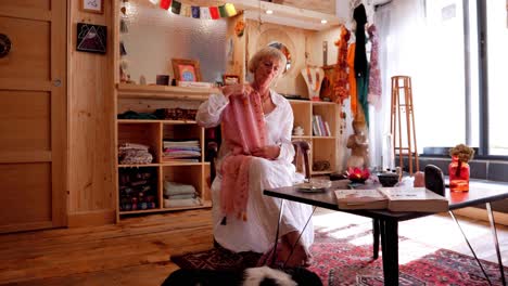 blonde woman adjusting her scarf in her spiritual living room with sleeping dog