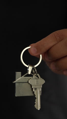 detailed close-up shot of a hand holding a house-shaped keychain, symbolizing buying a house. crisp lighting and focus highlight the metallic texture in this vertical video