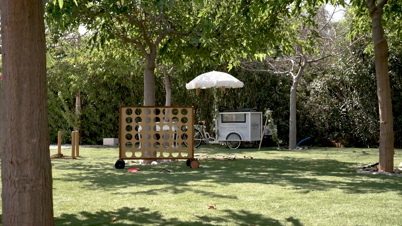 A family enjoys a sunny day playing a giant connect four game in a green park. Nearby, a food cart adds to the cheerful atmosphere with tasty treats for everyone.