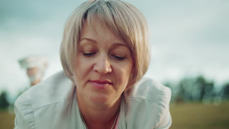 primer plano íntimo de una mujer tranquila y reflexiva con cabello gris, ojos suavemente cerrados, tendida en un vasto campo abierto, el fondo suavemente borroso, creando una atmósfera tranquila y meditativa