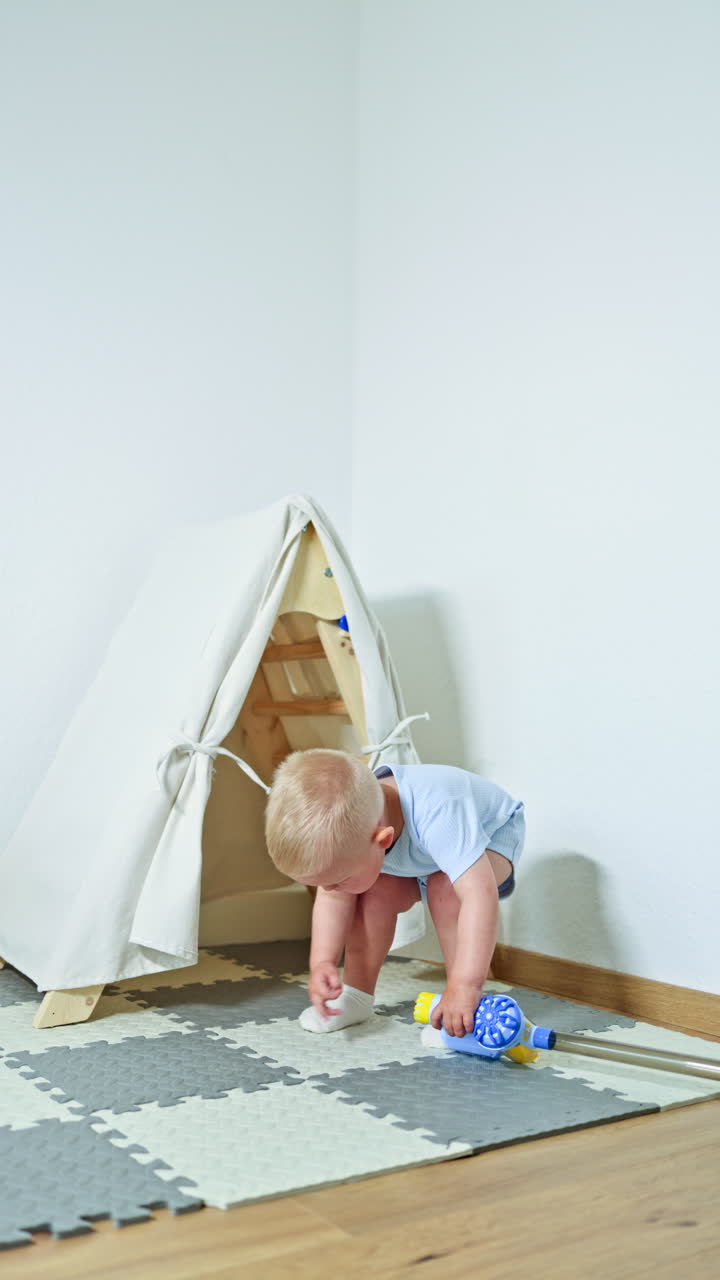 Cute boy 2 years old vacuuming at home. Toddler boy cleaning the room with a handheld vacuum cleaner. Child self-development, little helper in the housework