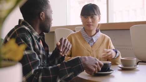 man and woman talking together and drinking cappuccino while sitting at table in a coffee shop