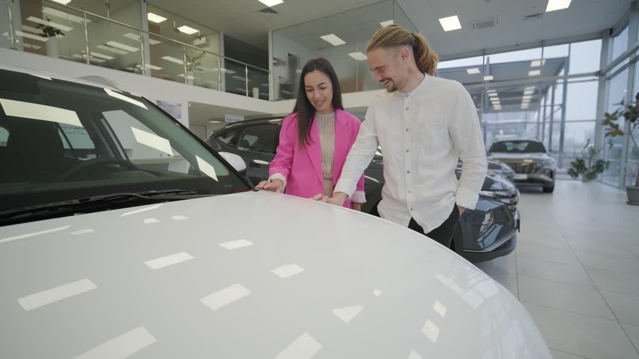 una hermosa pareja de jóvenes en la sala de exposición de automóviles eligiendo un coche nuevo para comprar.