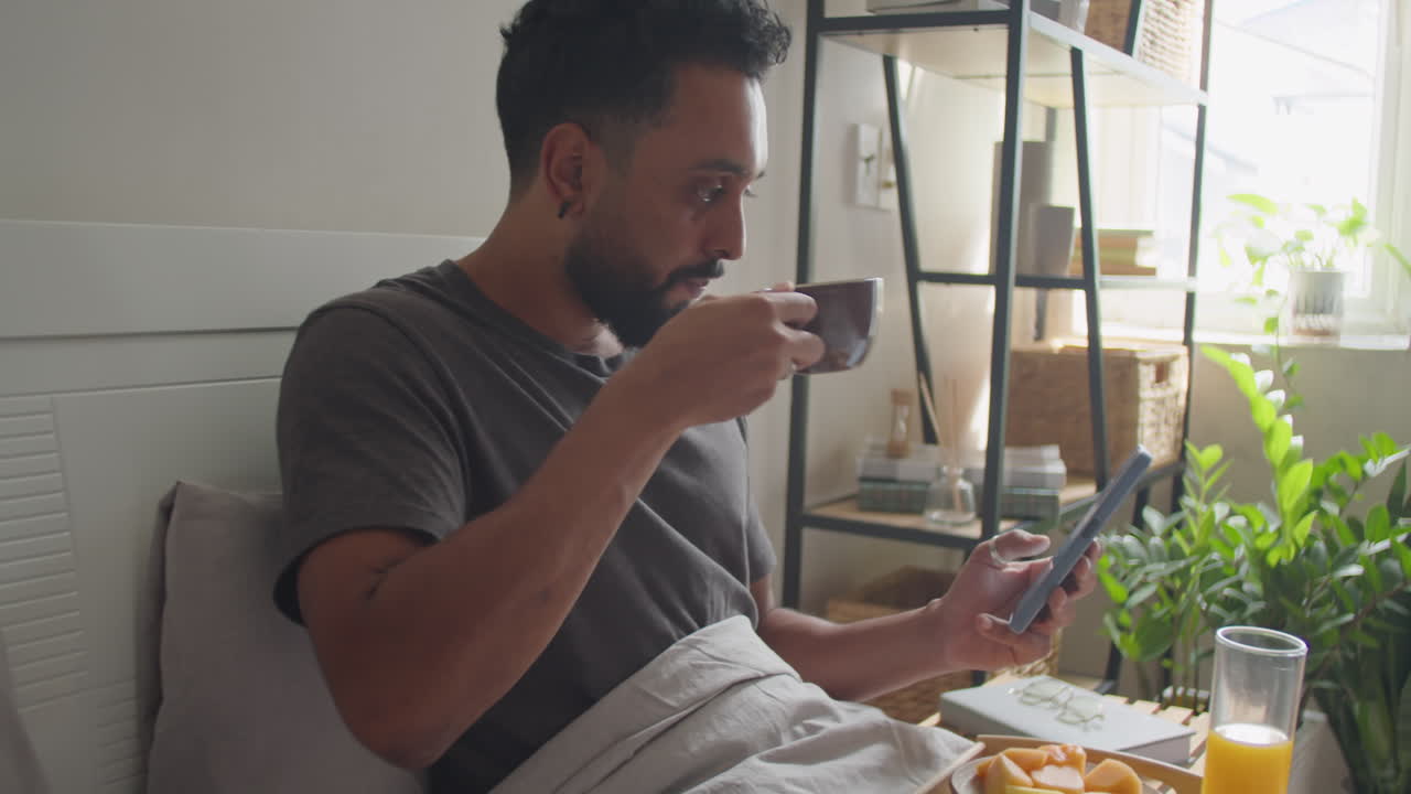 Man Using Smartphone and Having Breakfast in Bed