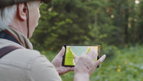 senior man using digital map on tablet in forest