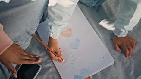 child hands coloring picture sitting on blanket outdoors with mother close up.