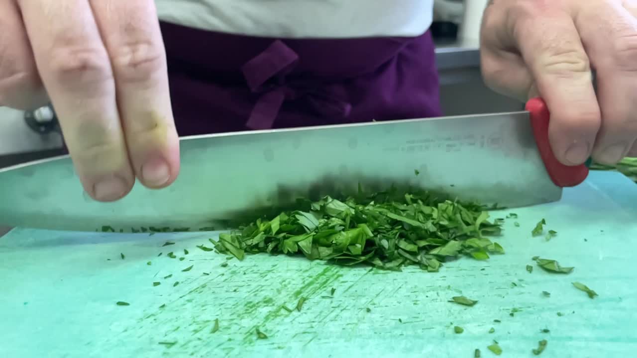 el chef corta y corta finamente las hojas de perejil verde en pedazos finos con un cuchillo de balanceo