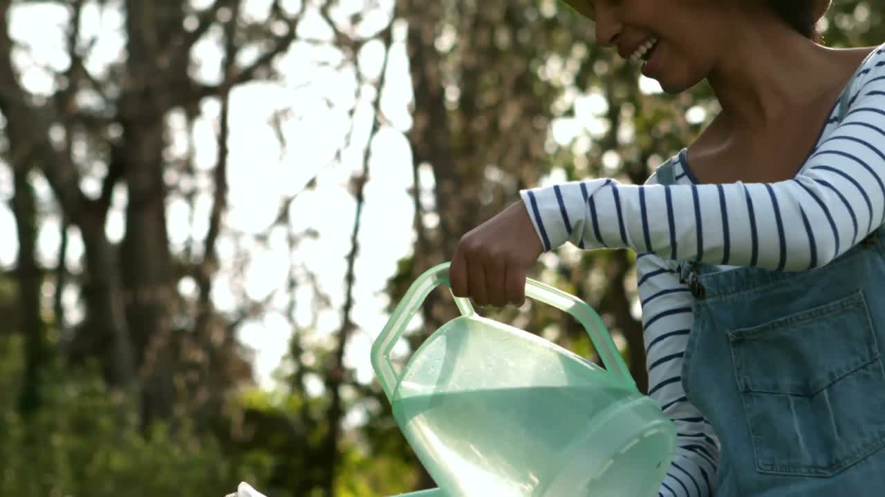 미소 짓는 정원사 여자 식물 에 물 을 주고 있다