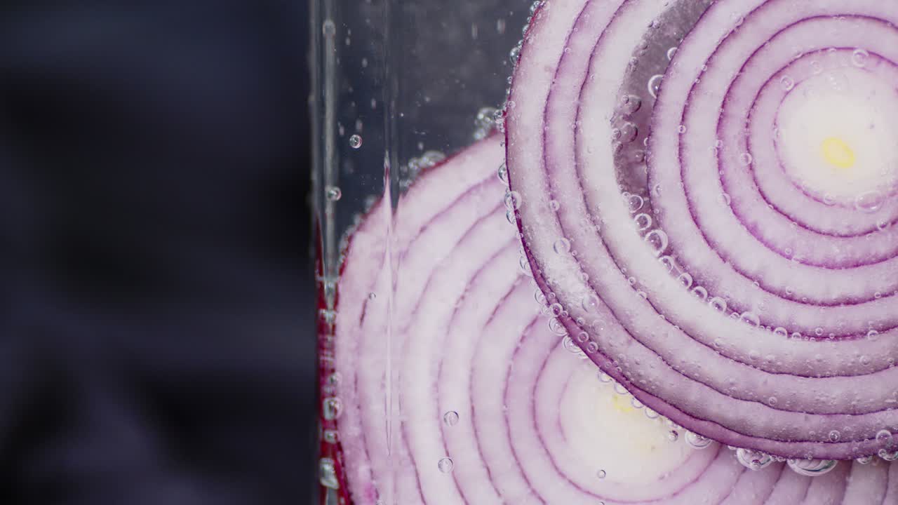 Round pieces of red onions under water with air bubbles.