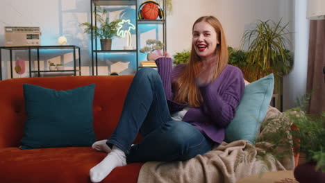 pretty woman smiling friendly at camera waving hands gesturing hello hi greeting at home on sofa