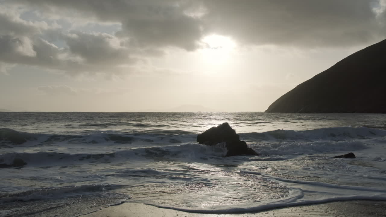 Wide shot of the ocean hitting a rock at keem bay in Ireland. Handheld slow motion shot with beautiful morning light from the sun.