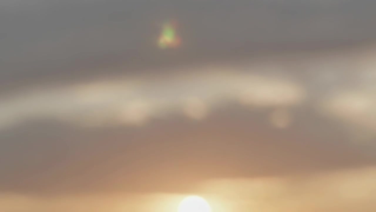 雲の層を突き抜け、外洋の空を太陽が明るく照らし、レンズフレアと反射を形成。