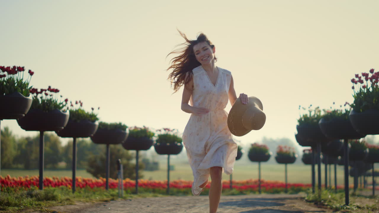 mujer joven corriendo en el parque con flores. chica feliz quitándose el sombrero.