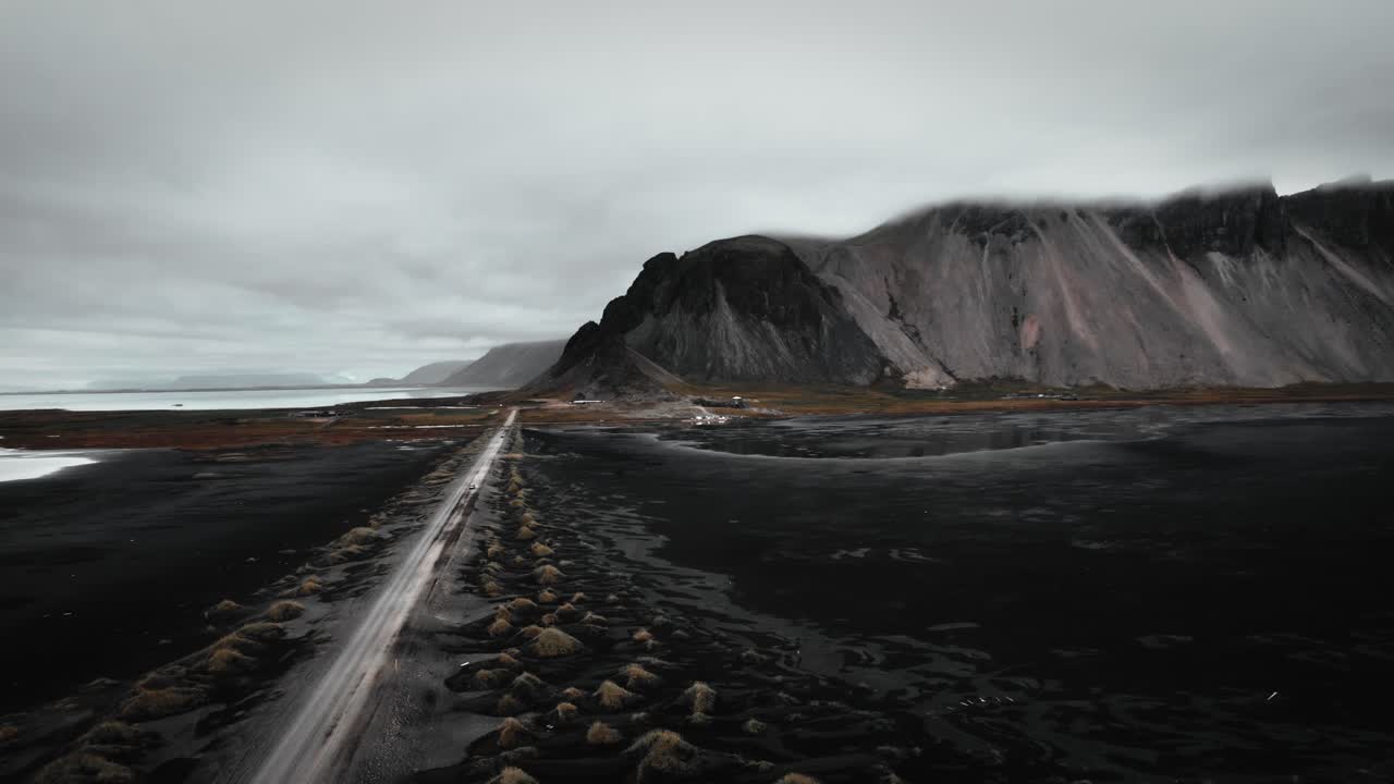 Aerial black sand beach stokksnes, volcanic dark mountains in distance, dark moody flying along road