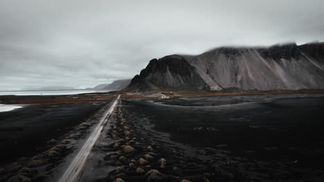 Playa-Aérea-De-Arena-Negra-Stokksnes,-Montañas-Volcánicas-Oscuras-En-La-Distancia,-Humor-Oscuro-Volando-A-Lo-Largo-De-La-Carretera