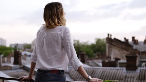 vista desde atrás de la hermosa mujer de pie en el balcón o terraza en el apartamento durante el día.joven dama disfrutando de la vista en el balcón de su habitación de hotel. pequeños edificios y casas vista