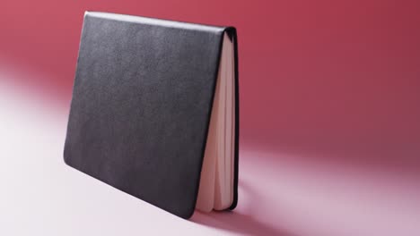 close up of open black book standing horizontal with copy space on red background in slow motion