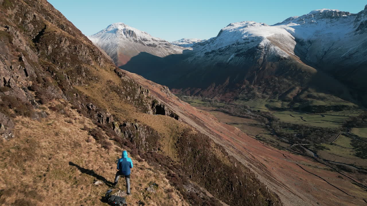volando sobre el excursionista en la ladera de la montaña revelando un valle verde con montañas nevadas en el distrito de los lagos wasdale uk
