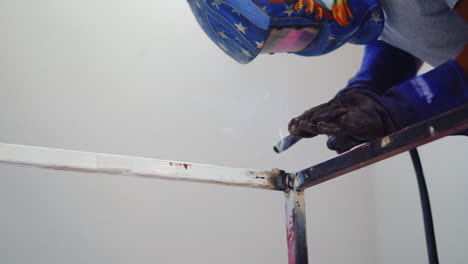 skilled welder in protective welding mask fabricating metal frame in a factory