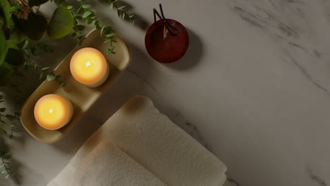 overhead view looking down on still life of lit candles and incense stick with green plant and towels as part of spa day decor 1