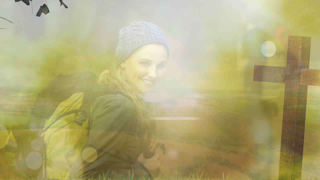 animación de una joven caucásica sonriente con mochila y cruz contra el sol brillante en el parque.