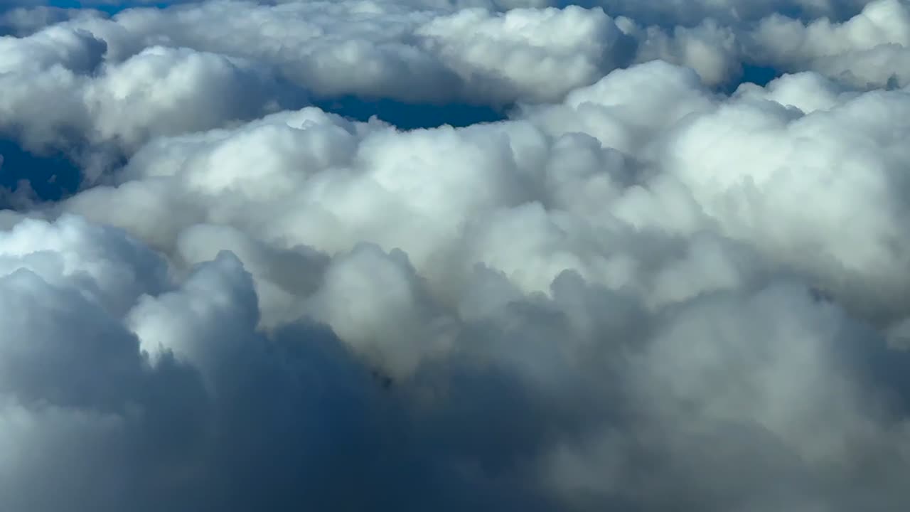 POV recorded from an airplane cockpit while flying at cruise above some cottony clouds at sunset
