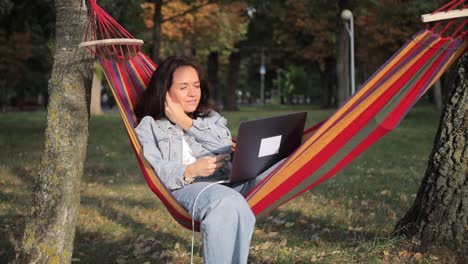 relaxing in a hammock blends work and leisure creating a peaceful moment to enjoy a woman finds joy while working on her laptop all while she relaxes in a comfortable hammock embraced by nature