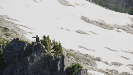 photographer takes selfie with camera on phone on mountain ridge with pine trees, tim durkan wide tracking helicopter counterclockwise orbit slow motion