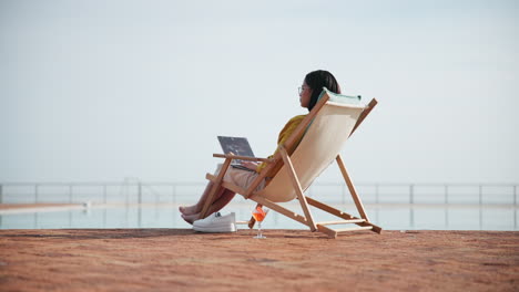 woman working on laptop by the pool with a cocktail