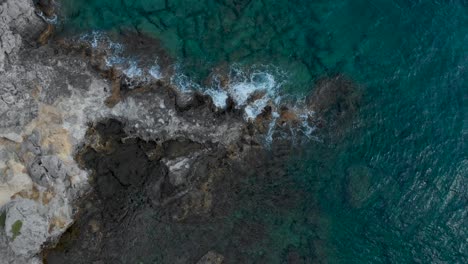aerial: drone flying down to fissured cliffs surrounded by waves and clear water