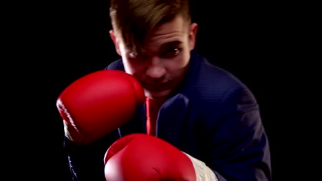 a young man of caucasian appearance in a suit raises his hands with boxing gloves and begins actively to dodge and sway before the fight