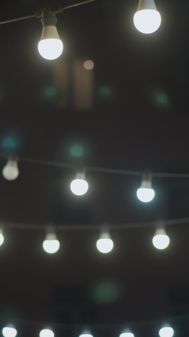 una acogedora escena al aire libre de la noche con luces de cuerda iluminando un camino alineado con bancos y una pared de ladrillo