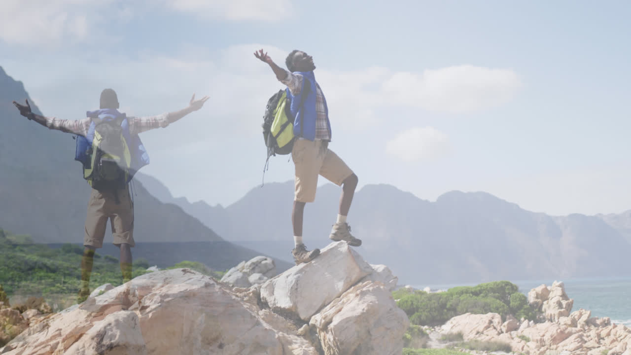 compuesto de un feliz hombre afroamericano caminando, y levantando los brazos en la ladera de la montaña