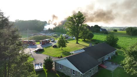 Aerial-Drone-View-Smoking-House-on-Fire,-American-Neighborhood,-Fumes-in-the-Sky-and-Fire-Trucks,-Countryside-Scenery-Establishing-Shot-at-Daylight