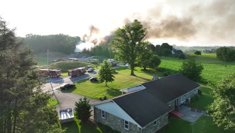 aerial drone view smoking house on fire, american neighborhood, fumes in the sky and fire trucks, countryside scenery establishing shot at daylight