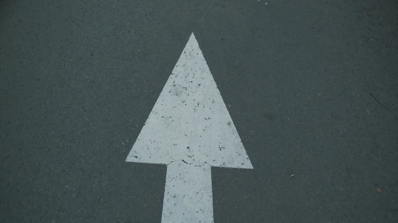 Indonesian white arrow road sign on an asphalt road.