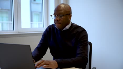 bald professional man working on laptop in a bright office environment, focusing on work