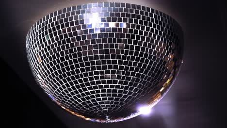 turning mirror disco ball against dark background. joy, dancing or party concepts. spinning mirror disco ball on the ceiling. close-up.