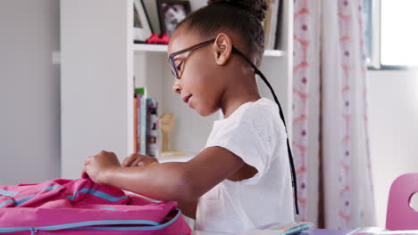 young girl wearing glasses packing bag for school in bedroom