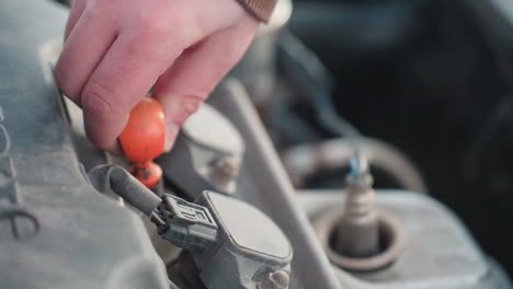 close up of person pulling dipstick from car engine bay to check oil level under raised hood during winter maintenance outdoors with frosty snow and engine parts visible in cold background