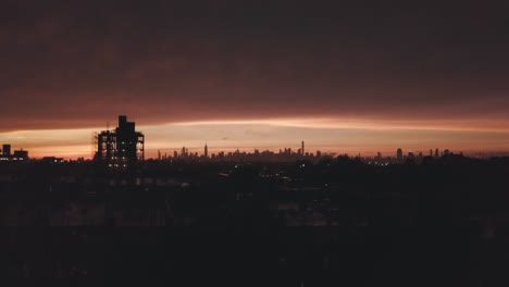 AERIAL:-Drone-Rising-Up-overlooking-Brooklyn-with-Manhattan-Skyline-in-Background-in-Dark-Orange-Dawn-Light