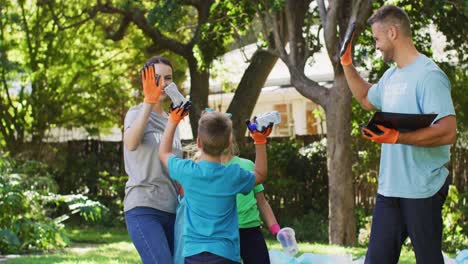 Lächelnde-Kaukasische-Eltern,-Sohn-Und-Tochter-Draußen,-Die-Plastikmüll-Sammeln-Und-High-Fiving-Machen