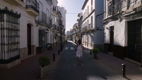 back view of a girl wearing white dress strolling through empty streets of olvera, spain